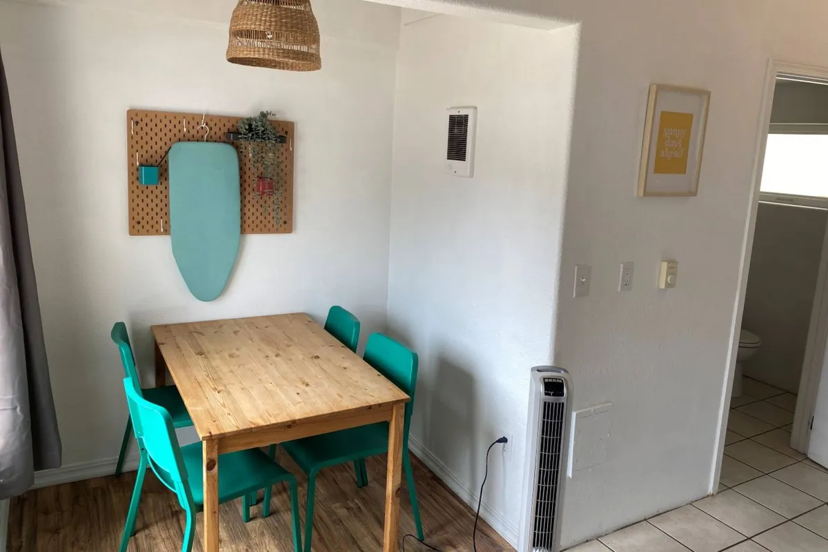 The image showcases a cozy dining area with a warm wooden table surrounded by inviting turquoise chairs, illuminated by a woven pendant light above. Decorative wall art adds charm, while the setup hints at shared moments over meals, celebrations, or creative activities.