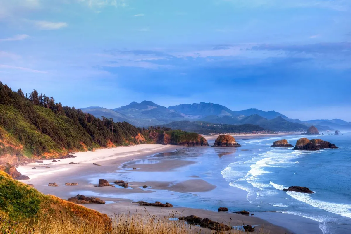 This image captures a scenic view of the nearby beach and ocean, with distant mountains and unique rock formations visible on the horizon. The atmosphere is peaceful, inviting thoughts of picnicking, photography, and enjoying the cool ocean breeze.